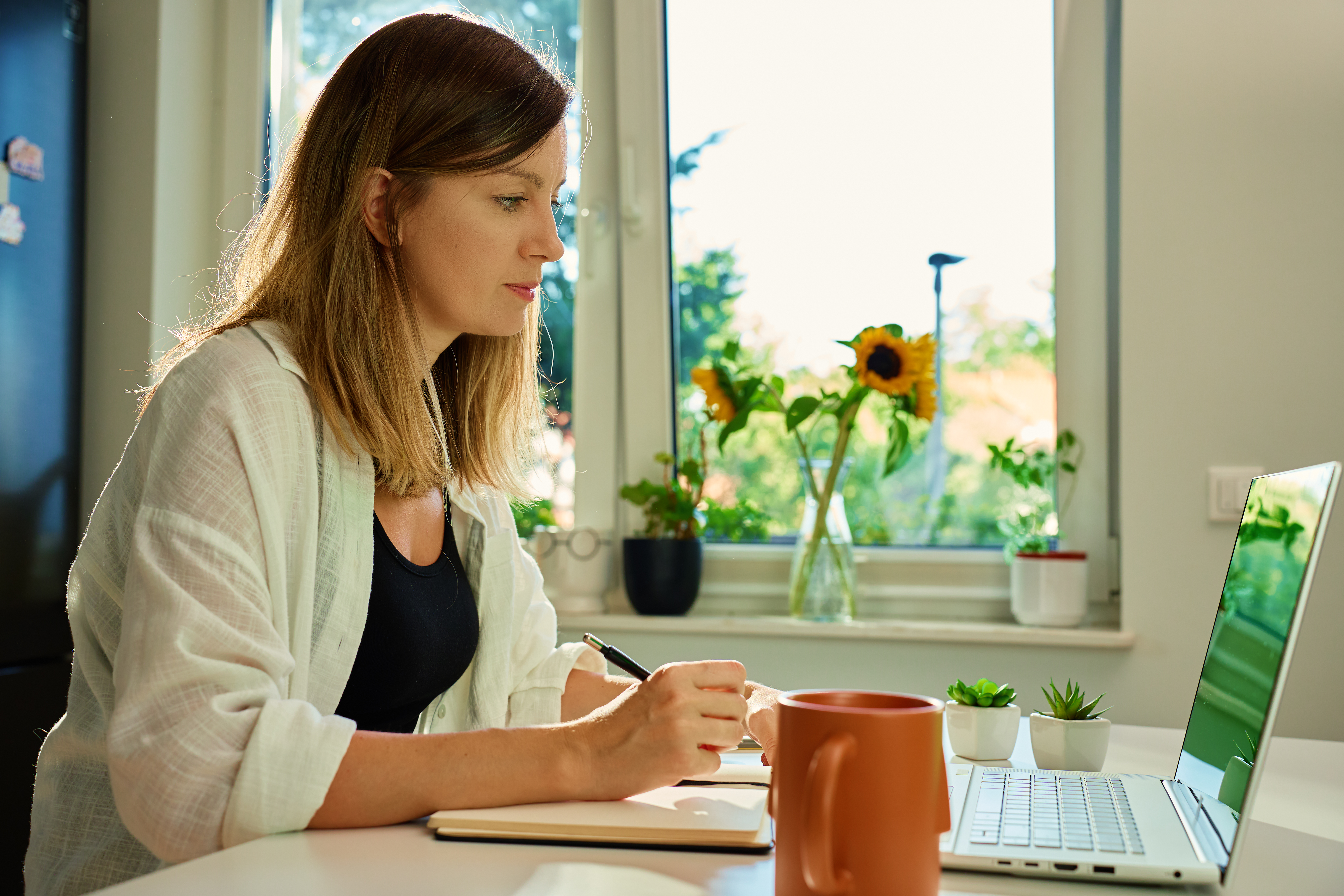 Woman using a notebook and laptop while organizing financial records at home